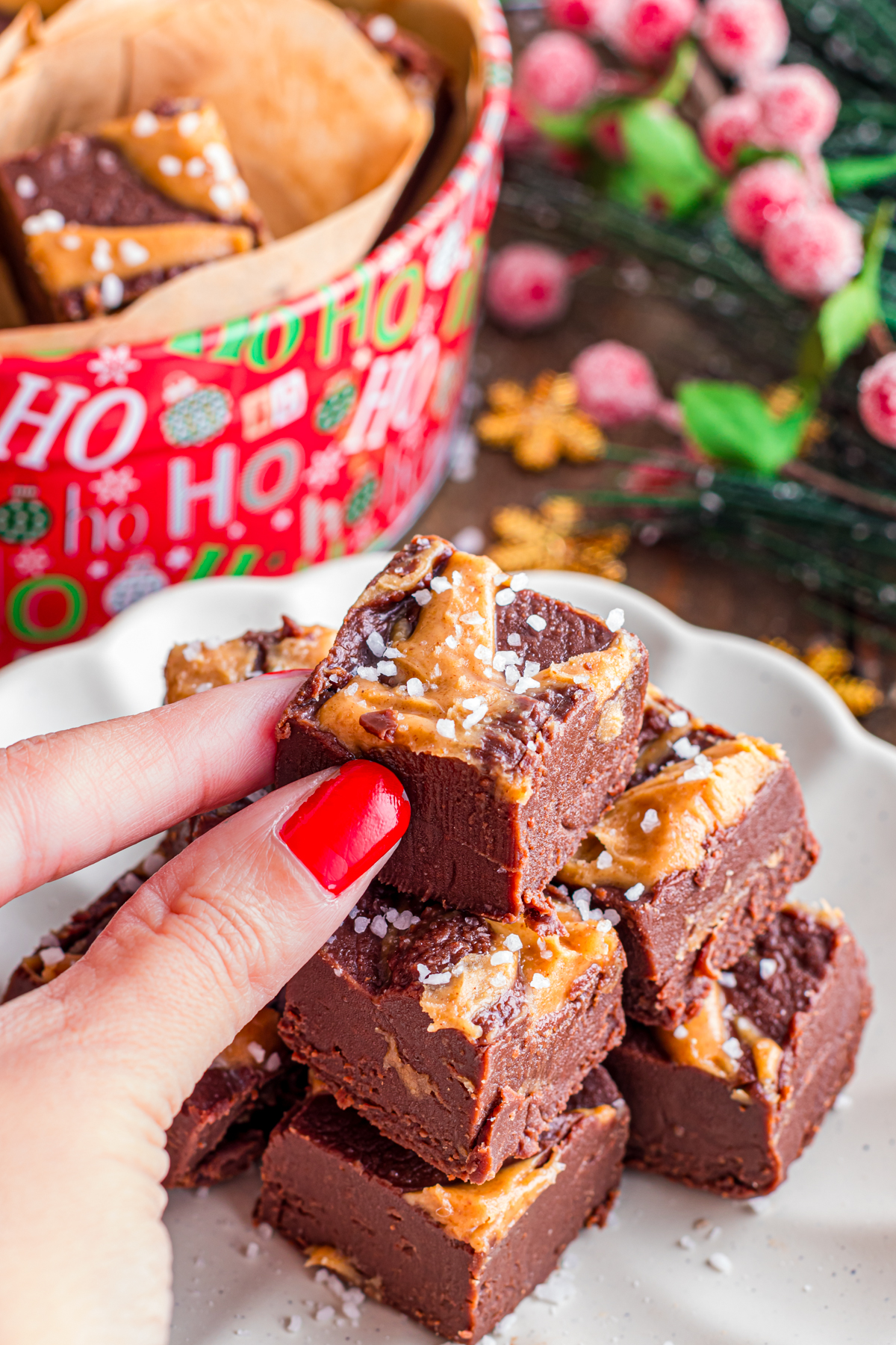 A hand with curly red nails holding a square of chocolate peanut butter fudge.