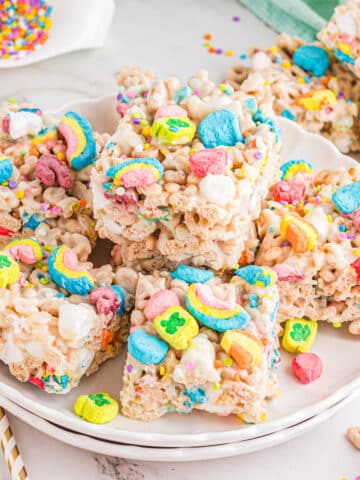 Lucky charms rice krispie treats stacked on a white scalloped plate.