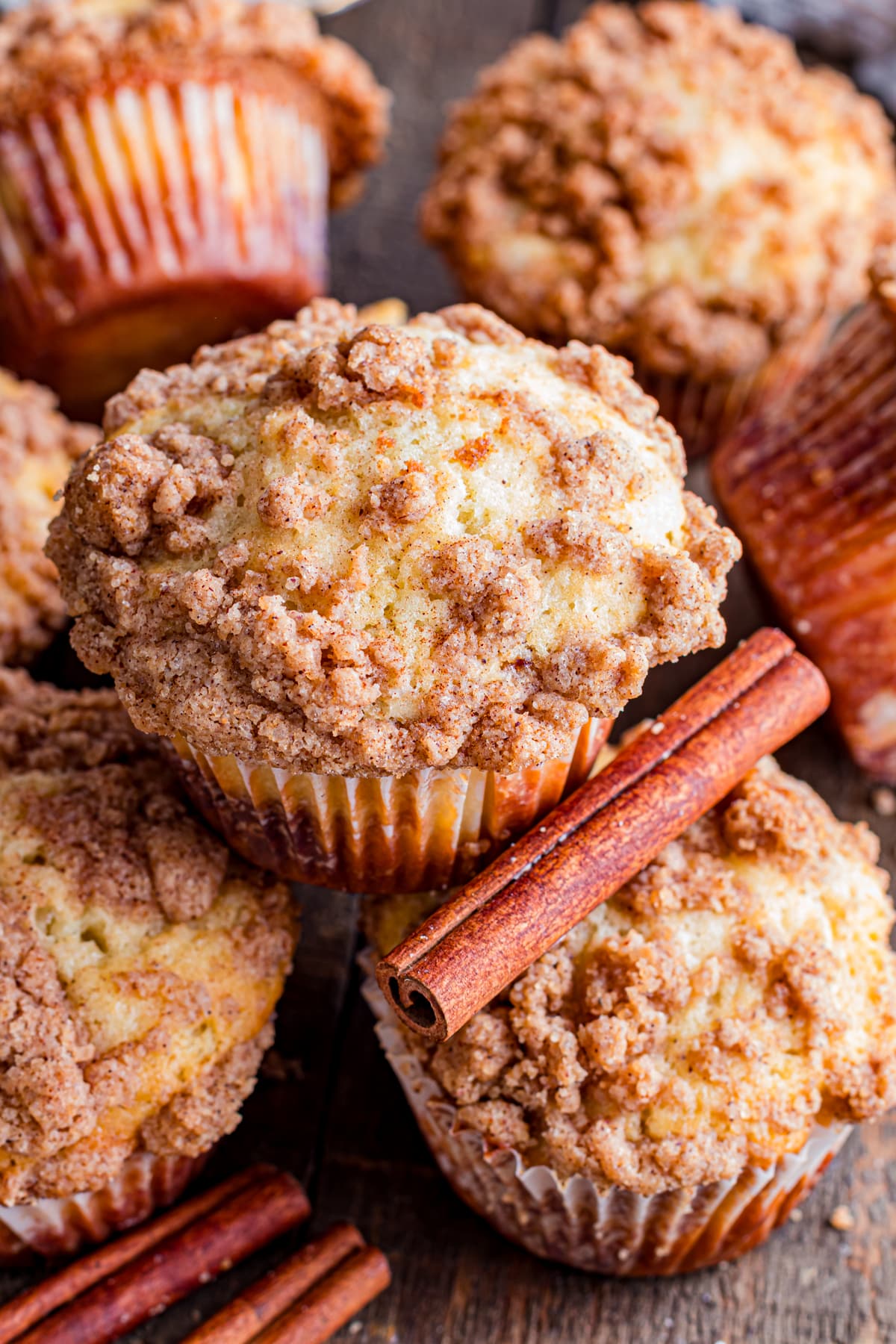 Cinnamon streusel muffins stacked on wood table with cinnamon sticks.